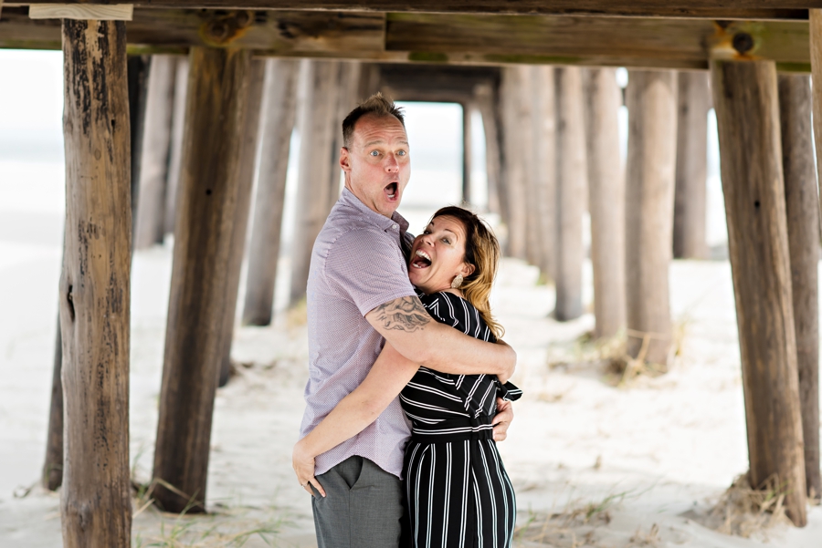 A woman grabs her fiance's butt under the pier during their cape may engagment session.